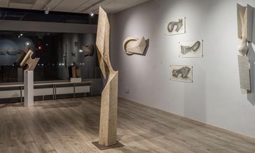 Zwei Holz-Skulpturen stehen im Raum, mehrere hängen an der weißen Wand